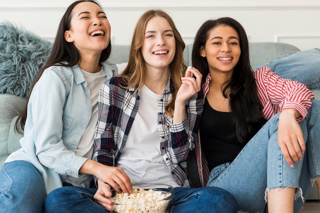 Laughing friends sharing bowl of popcorn