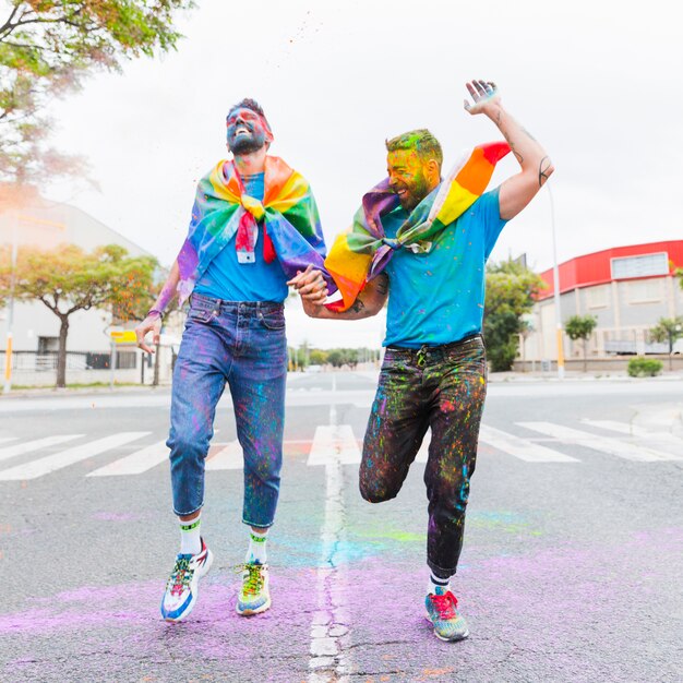 Laughing gay couple running on road with rainbow flag