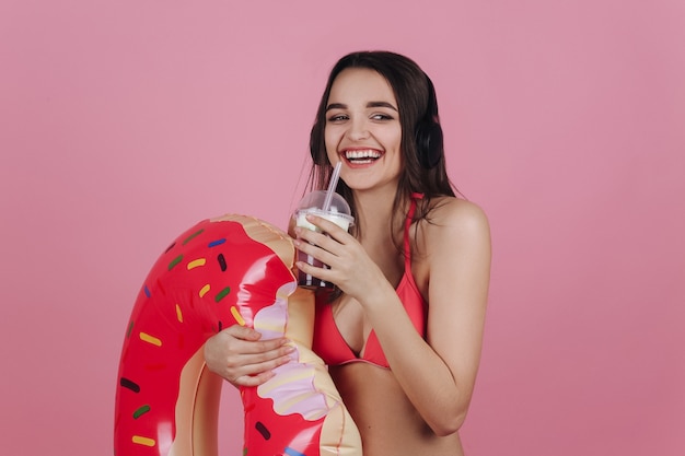 Laughing girl in beach dress stands with a cocktail and big donut swim ring