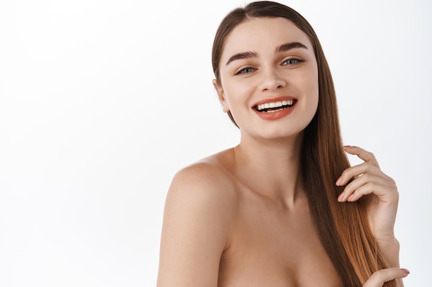 Laughing girl brushing hair strands with hand and smiling at front