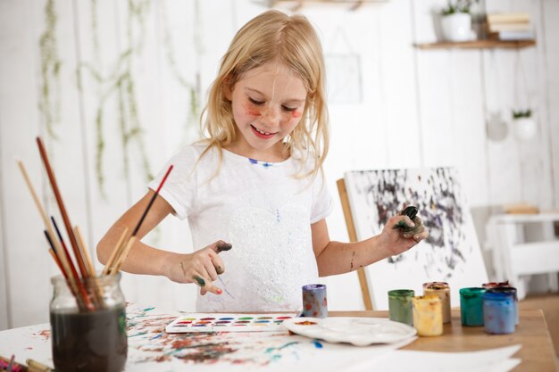 아트 룸에서 페인트에 손으로 기쁨 가득한 웃는 소녀. 미소로 명랑 한 아이 그림 그리기. 유쾌한 아이는 긍정적 인 감정과 행복을 발산합니다.