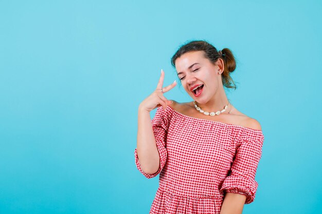 Laughing girl is closing eyes and showing two gesture on blue background