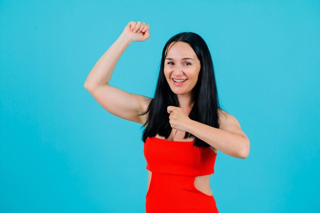 Laughing girl is dancing y raising up her fists on blue background