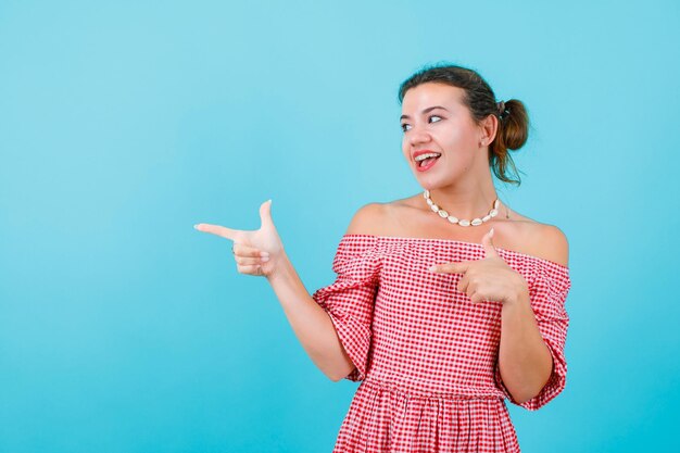 Laughing girl is looking and pointing left with forefinegrs on blue background