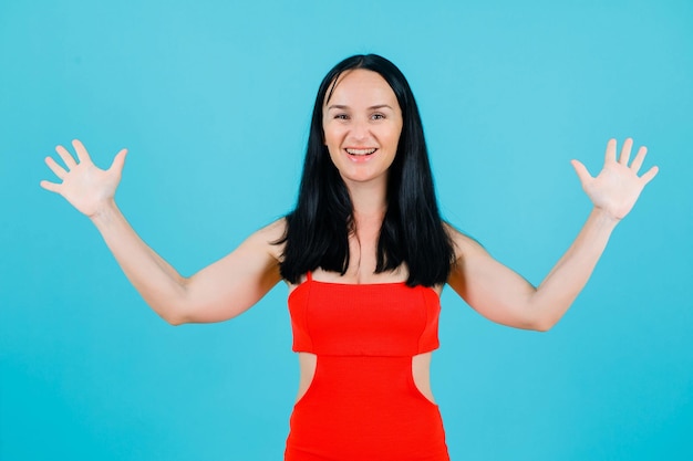 Laughing girl is opening wide her arms by raising up them on blue background