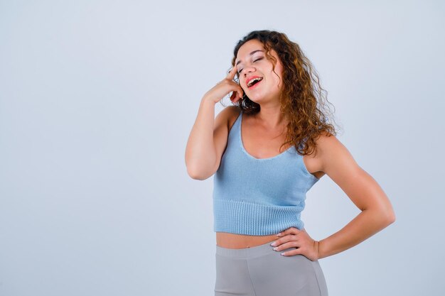 Laughing girl is wishing by holding forefinger on temple on white background