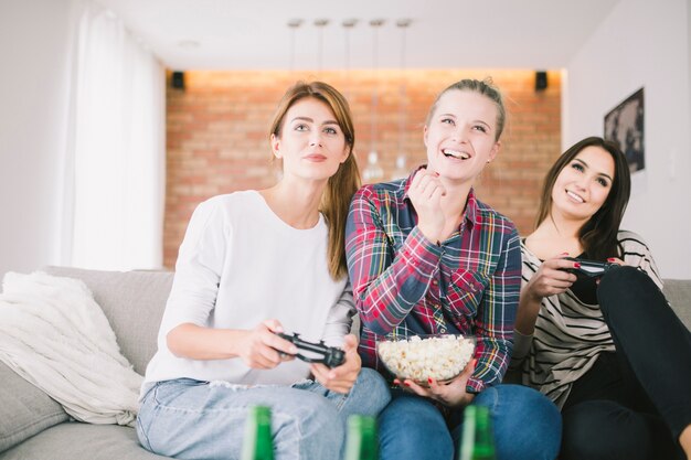 Laughing girlfriends playing videogame and having beer