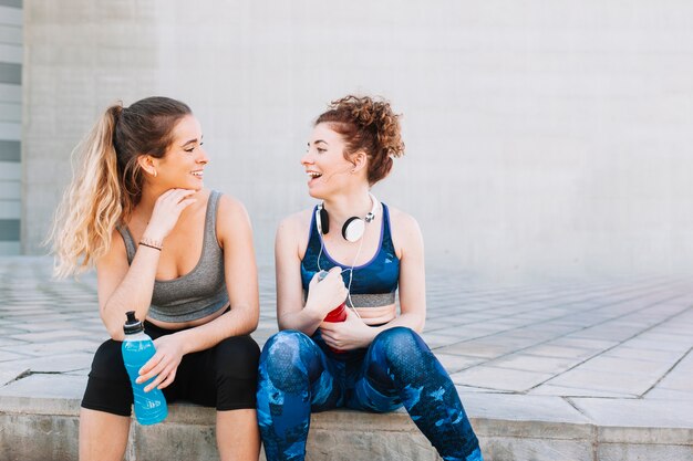 Laughing girls in sportswear sitting on street
