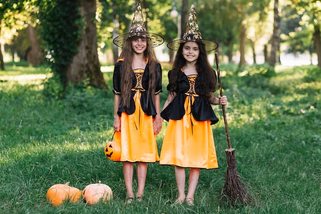 Ragazze ridenti in costumi strega che si tengono per mano, scopa e zucca