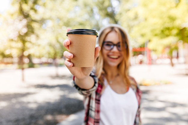 公園でラテを飲むゴージャスな女の子を笑う。手前にコーヒーのカップと金髪の女性のぼやけた肖像画。