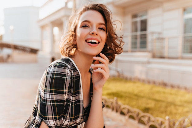 Foto gratuita ridendo splendida donna con la pelle pallida in posa sulla strada di sfocatura. giovane signora vaga di buon umore trascorrere del tempo all'aperto.