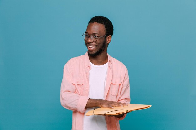 Смеющийся молодой афроамериканец, держащий папку на синем фоне