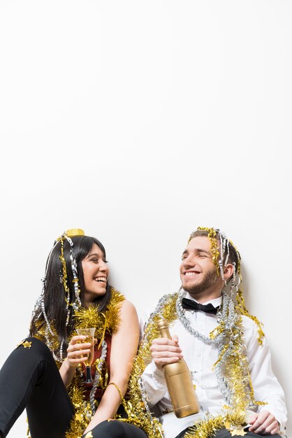 Laughing lady and guy in evening wear and tinsel with bottle and glass 