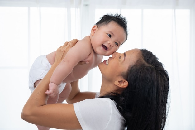 空中で彼女の愛らしい生まれたばかりの赤ちゃんの息子を持ち上げて笑う母親