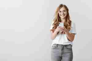 Free photo laughing over picture girl took. portrait of happy attractive caucasian female blogger in glasses and trendy outfit holding smartphone, chuckling from positive emotions