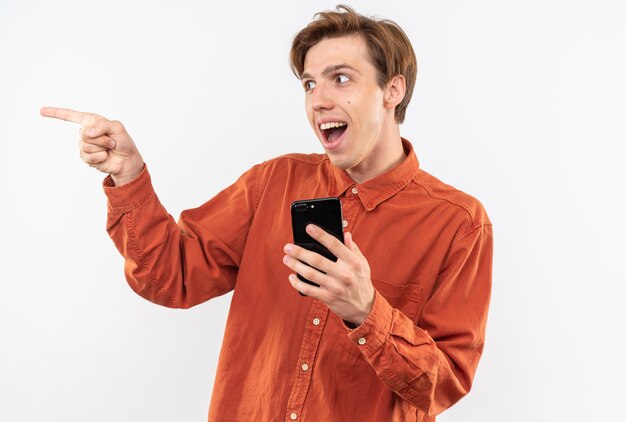 смеющиеся точки сбоку молодой красивый парень в красной рубашке держит телефон изолирован на белой стене