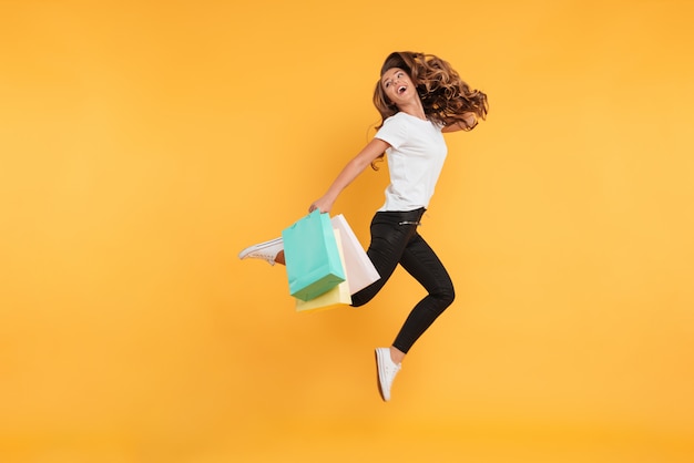 Laughing pretty young woman jumping holding shopping bags.