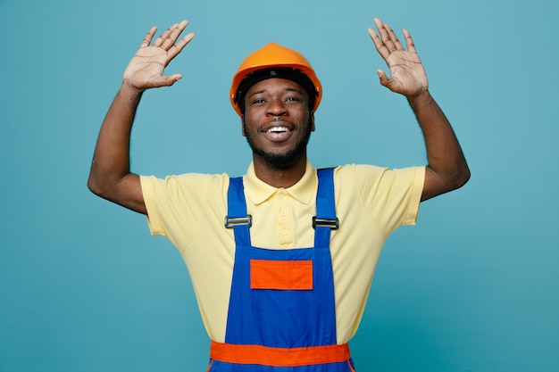 Laughing raised hand young african american builder in uniform isolated on blue background