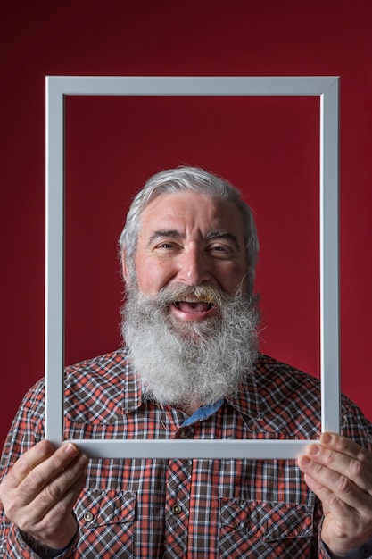 Laughing senior woman holding white frame border in front of his face against red backdrop