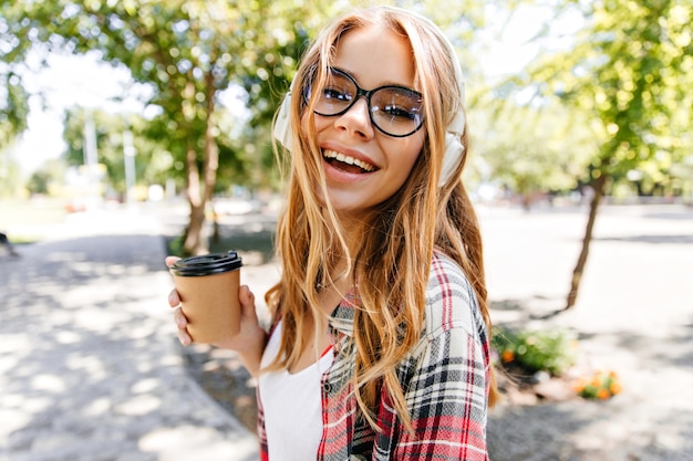 Donna spettacolare di risata che gode del tè nel parco. elegante ragazza caucasica che beve caffè sulla natura.