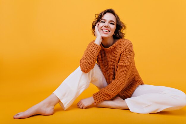 Laughing stunning girl in cozy sweater sitting on the floor
