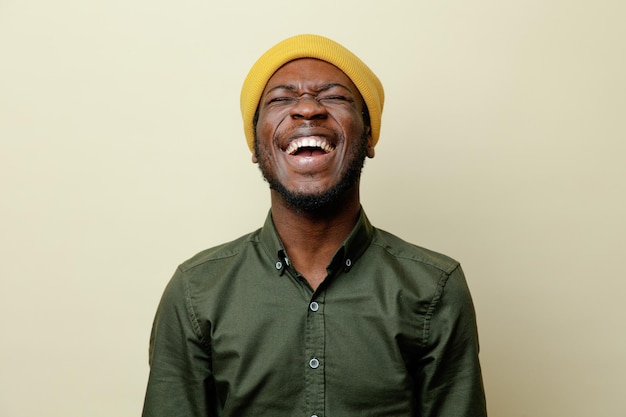 Laughing with closed eyes young african american male in hat wearing green shirt isoloated on white background