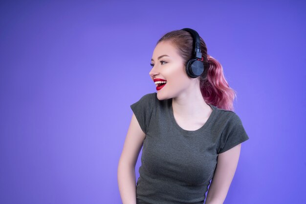 Laughing woman in a gray t-shirt enjoys music from the headphones