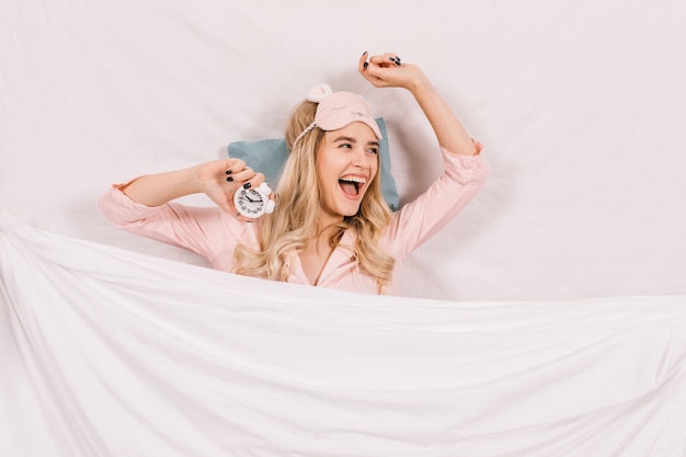 Laughing woman in sleep mask lying in bed