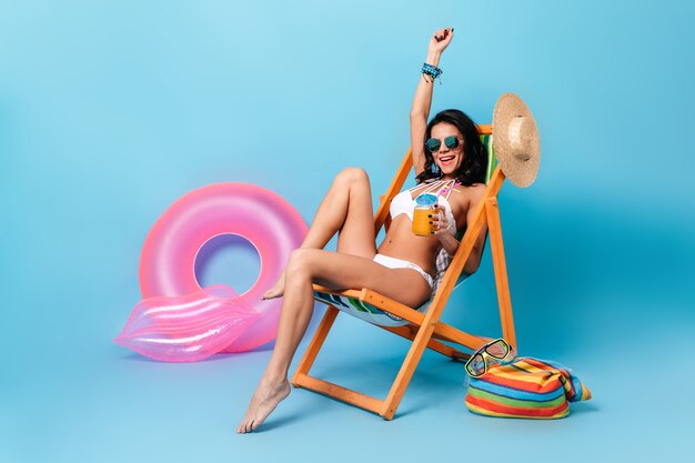 Laughing woman in sunglasses sitting on deck chair with hand up