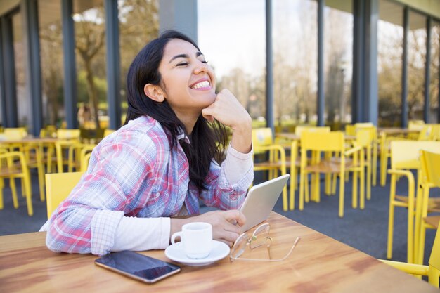 Laughing woman using gadgets and drinking coffee in cafe