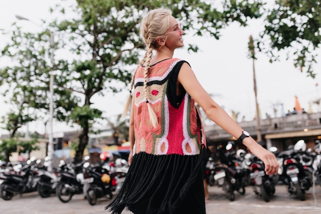 Foto gratuita donna che ride con lunghe trecce bionde. colpo esterno di graziosa donna abbronzata indossa abiti colorati a maglia.