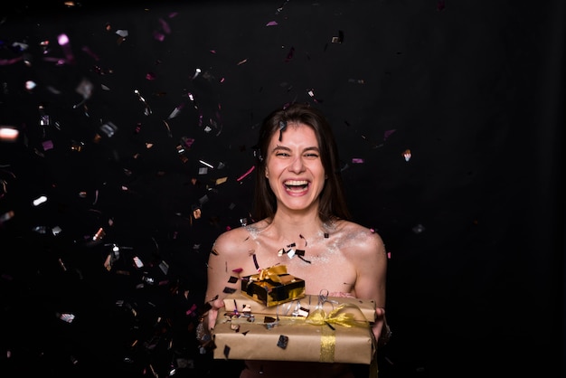 Laughing woman with present boxes between confetti 