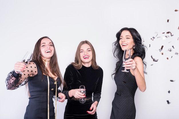 Laughing women in evening wear with glasses near confetti 