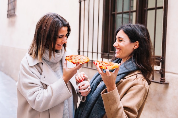 Free photo laughing women having pizza on street