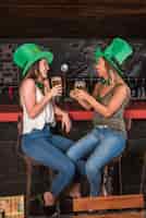 Foto gratuita donne che ridono in cappelli di saint patricks con bicchieri di drink al bancone del bar