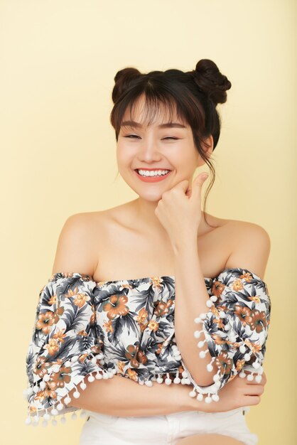 Laughing young Chinese girl with closed eyes, in bare shoulder top posing in studio