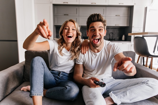 Laughing young people sitting on couch. Smiling family watching TV.