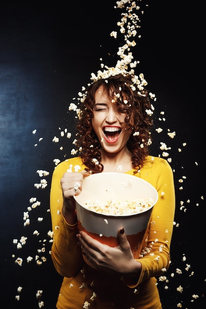 Laughing young woman staying under cheesy popcorn shower at cinema