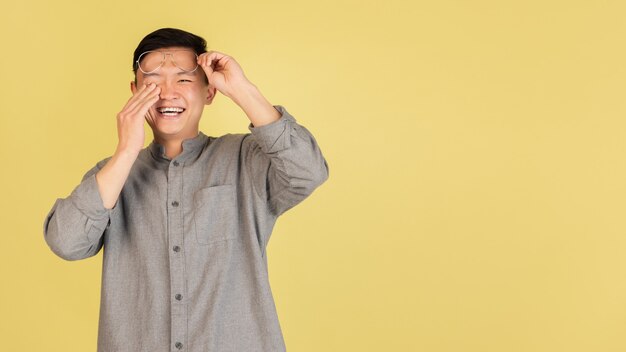 Laughting. Asian young man's portrait on yellow  wall. Handsome male model in casual style. Concept of human emotions, facial expression, youth, sales, ad.