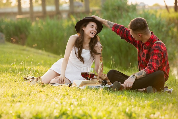 Смеется. Кавказская молодая, счастливая пара, наслаждаясь выходными вместе в парке в летний день