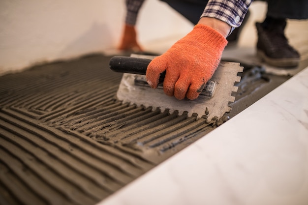 Laying Ceramic Tiles. Troweling mortar onto a concrete floor in preparation for laying white floor tile.