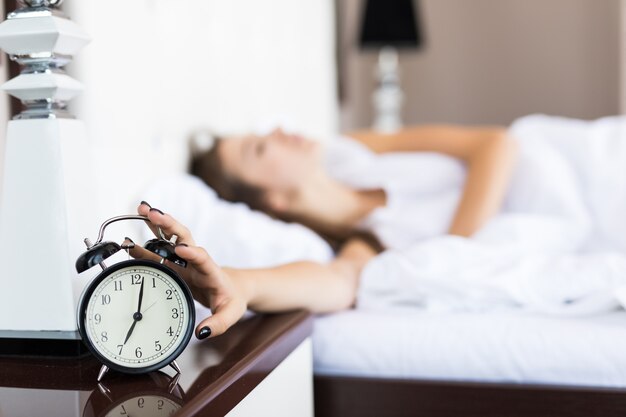 Lazy woman continue to lie after alarm clock ringing in the morning