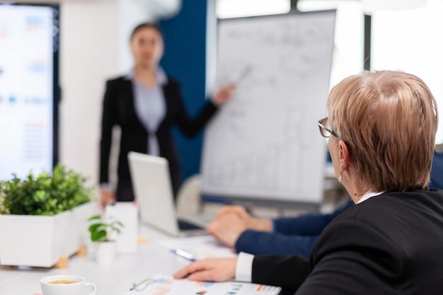 Leader making sales report for top company managers drawing charts on white board. Serious speaker boss executive, business trainer explaining development strategy to motivated mixed race employees.