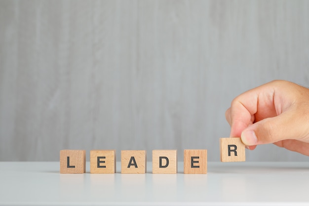 Leadership concept on grey and white table side view. hand picking up wooden cube.