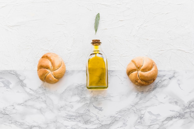 Leaf over the olive oil bottle with two round buns on two textured background