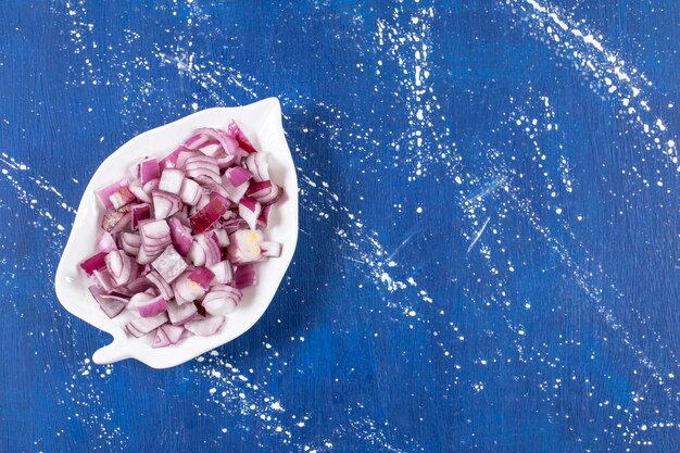 Leaf-shaped plate of sliced purple onions on marble surface. 