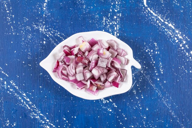 Leaf-shaped plate of sliced purple onions on marble table.