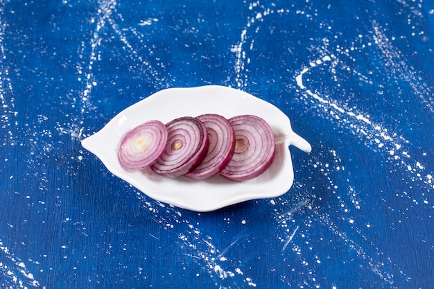 Leaf-shaped plate with purple onion rings on marble surface