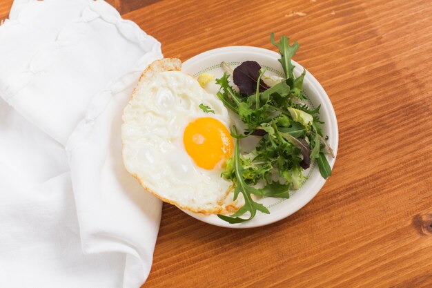 Leafy vegetables and half fried eggs on plate over the wooden desk