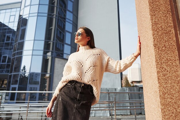 Leaning on the wall by hand. Young beautiful girl in warm clothes have walk in the city at her weekends time